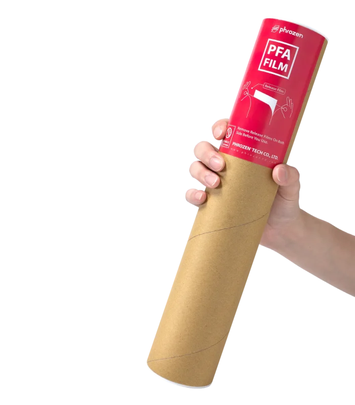 Hand holding a red cylindrical canister labeled 'PFA FILM' (release film) against a light background, with a brown paper core showing at the bottom field guide.