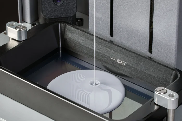 Close-up of a white optical disc being loaded into a metal device with clamps and a MAX indicator visible in the tray.